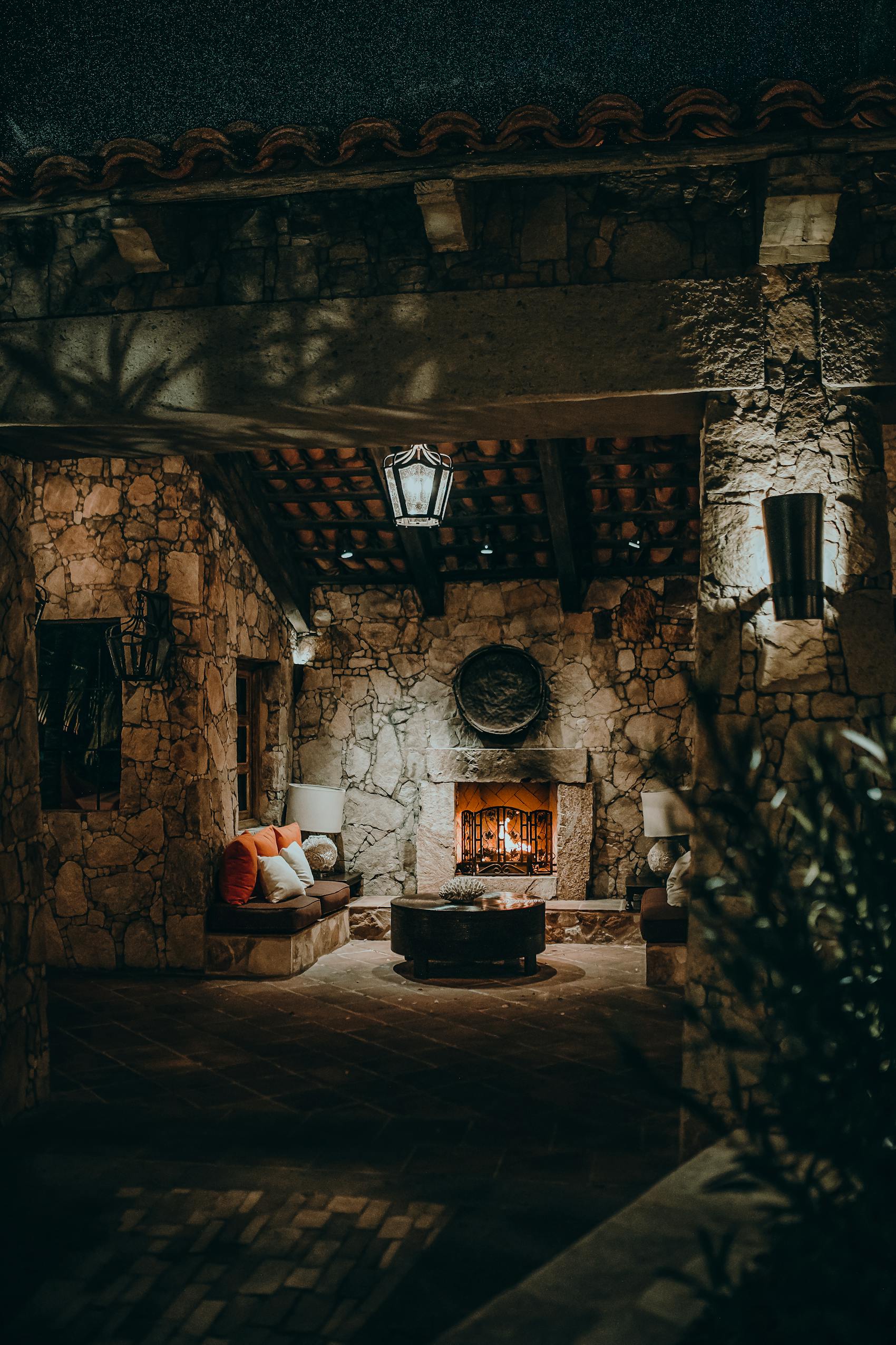 Glowing stone fireplace in a hand-built stone courtyard at dusk